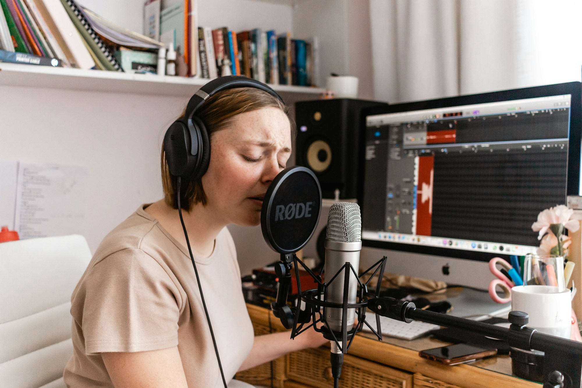 Una cantante grabando con micrófono y auriculares, con una pantalla de análisis de audio al fondo